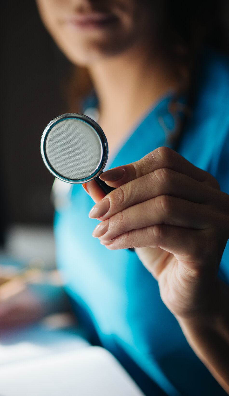A clinician holding a stethoscope in a softly lit consult room